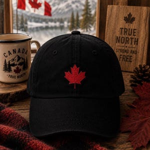 May include: A black baseball cap featuring a red embroidered maple leaf centered on the front panel. The cap has a structured crown and a curved brim, showcasing a classic design with a prominent red maple leaf emblem stitched onto the fabric.