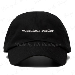 May include: A black baseball cap with the text "voracious reader" in white lettering. The cap has a curved brim and a black adjustable strap.