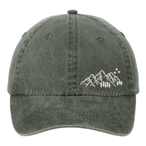 May include: A dark green baseball cap with a mountain and star design. The white graphic features a mountain range and trees. The cap has a curved brim and an adjustable strap.