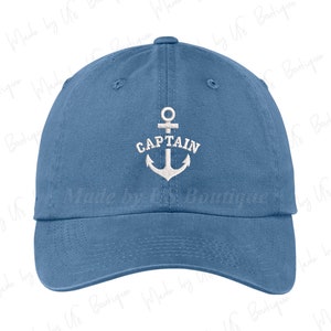 Könnte beinhalten: Blaue Baseballkappe mit weiß gesticktem Anker und dem Wort "CAPTAIN". Die Kappe hat einen gebogenen Schirm und einen verstellbaren Stoffriemen. Der Hut ist aus einem weichen, strapazierfähigen Material gefertigt.