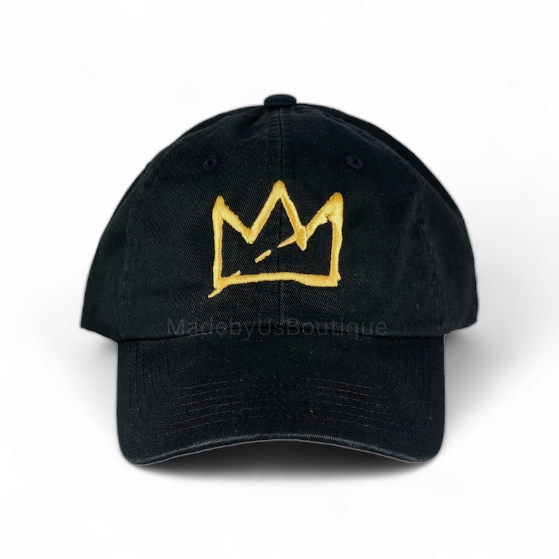May include: Black baseball cap with a gold embroidered crown design. The text "MadebyUsBoutique" is embroidered on the front of the cap.