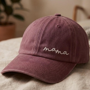 May include: A dusty rose baseball cap with the word "mama" embroidered in white script. The cap has a curved brim and a classic six-panel design, perfect for casual wear.