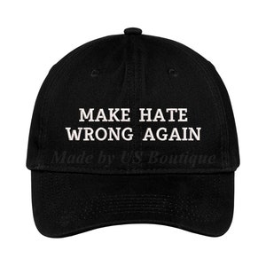 May include: Black baseball cap featuring the embroidered phrase "MAKE HATE WRONG AGAIN" in white. The cap has a curved peak and a structured crown. The text is centered on the front. The words "Made by US Boutique" are printed below the text.