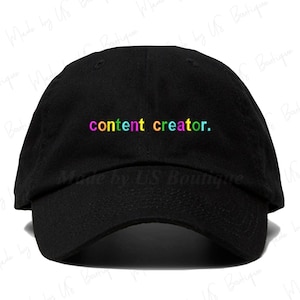 May include: Black baseball cap with the text "content creator." in rainbow colours.