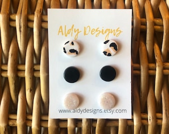 May include: A set of six stud earrings on a white card with the text "Aldy Designs" and the website "www.aldydesigns.etsy.com". The earrings are in three different designs: black, white with a glitter finish, and white with a leopard print.