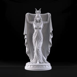 Peut inclure: Une statue blanche repr&eacute;sentant une silhouette debout v&ecirc;tue d'une longue robe fluide et d'une coiffe orn&eacute;e d'un croissant de lune et d'une sph&egrave;re centrale. La silhouette tient un grand drap&eacute; d&eacute;ploy&eacute; avec ses deux bras sur un socle circulaire.
