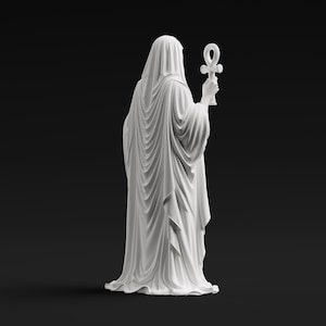 May include: A matte white statue of a cloaked figure viewed from behind, draped in flowing, detailed fabric that falls to the base. The figure holds an ankh symbol upright in one hand, with the entire sculpture presented against a solid black background.