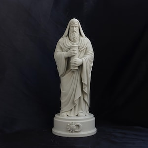 May include: A light grey statue of a bearded figure wearing a hooded robe and a winged collar, holding a cylindrical scroll. The figure stands on a circular base featuring a sun and crescent moon emblem embossed on the front surface.