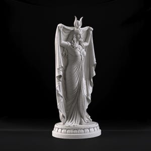 Peut inclure: Une statue en pierre gris clair repr&eacute;sentant une silhouette debout v&ecirc;tue d'une longue robe fluide et d'une coiffe orn&eacute;e d'un croissant de lune et d'un disque solaire. La silhouette tient un grand drap&eacute; au-dessus de sa t&ecirc;te, pos&eacute;e sur un socle.