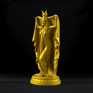 Peut inclure: Une statue dor&eacute;e repr&eacute;sentant une silhouette debout v&ecirc;tue d'une longue robe fluide et d'une coiffe en forme de croissant de lune. La silhouette tient un grand morceau de tissu drap&eacute; au-dessus de sa t&ecirc;te avec ses deux bras, sur un socle circulaire.