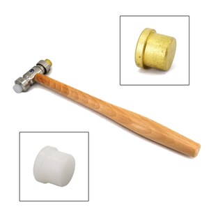 May include: A small, light-colored wooden-handled hammer with a metal head and interchangeable white and yellow striking surfaces. Two close-up inset images show a brass head and a white striking surface.