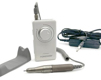 May include: A white and gray portable Foredom nail drill kit. The kit includes a control box with a dial, a handpiece, a gray cradle, and a power adapter. The handpiece is gray and silver. The text "FOREDOM" is printed on the control box.
