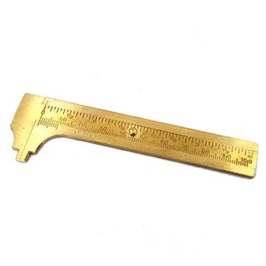 May include: A brass ruler with a sliding caliper, marked in inches and 1/16ths of an inch. The ruler is 6 inches long.