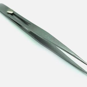 Può includere: Una pinzetta argentata con una punta appuntita. La pinzetta ha un piccolo pomo rotondo argentato in cima.