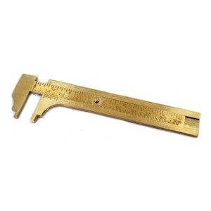 May include: A brass caliper with a ruler marked in inches and centimeters. The ruler is marked up to 4 inches or 10 centimeters.
