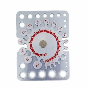 May include: A silver metal ring gauge with a circular scale marked in millimeters and fractions of an inch. The gauge has a series of holes of different sizes for measuring rings.