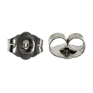 Peut inclure: Deux fermoirs d'oreilles argentés. L'un est de style papillon, l'autre est de style poussoir rond. Les deux sont en matériau métallique brillant. Le fermoir papillon a une surface texturée.