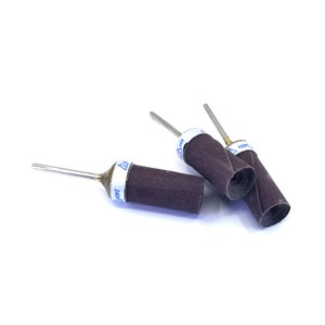 May include: Three brown sanding drums with metal shafts and white labels. The labels have a blue triangle warning symbol and the text "240#", "180#", and "120#" printed on them.