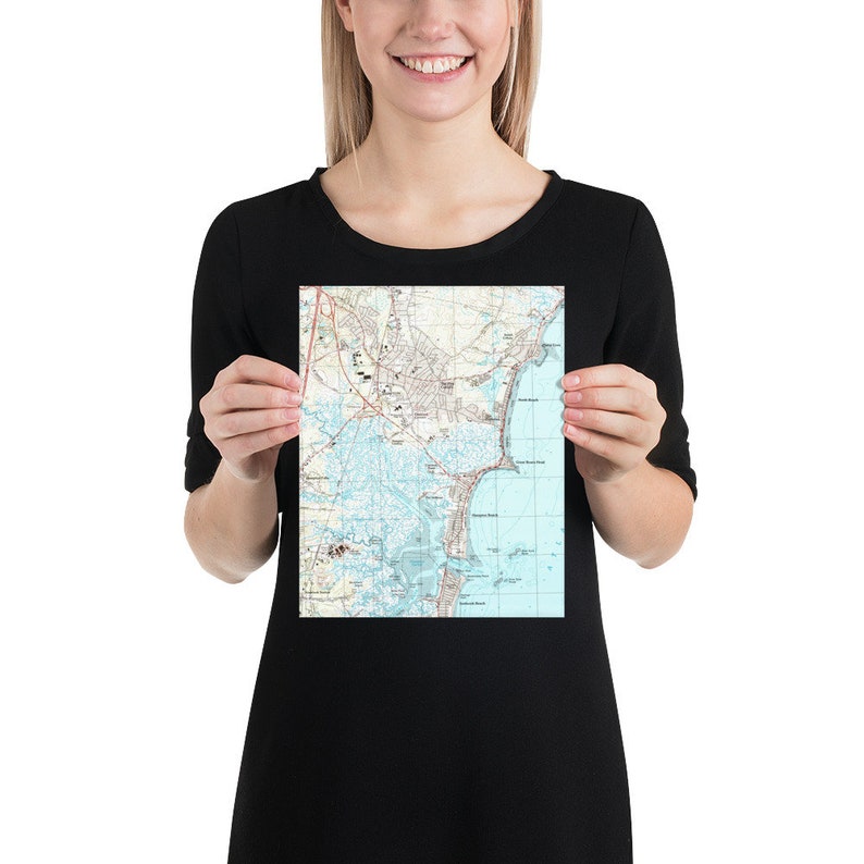 May include: A person holding a vintage map print of a coastal city. The map shows streets, waterways, and landmarks. The map is printed on white paper with blue and brown lines.