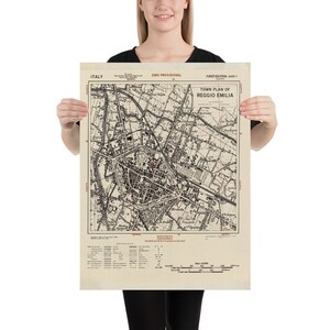 Op de afbeelding: Een vintage kaart van Reggio Emilia, Italië, gedrukt op verouderd papier. De kaart, getiteld "Town Plan of Reggio Emilia", toont gedetailleerde straatindelingen, gebouwen en geografische kenmerken. De kaart bevat tekst in het Engels en Italiaans.