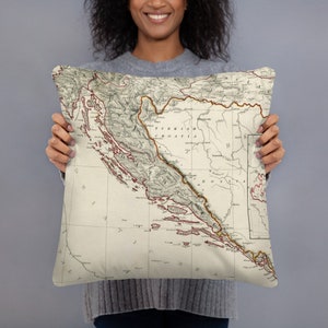 May include: A throw pillow featuring a vintage map of Turkish Croatia. The map is printed on a cream-colored fabric with brown and red lines and text.