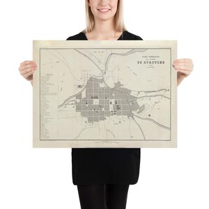 Peut inclure: Une carte ancienne d'Ayacucho, Pérou, en noir et blanc. La carte, tenue par une personne, présente une planification urbaine détaillée, des rues et des bâtiments. Le titre "PLANO TOPOGRAFICO DE AYACUCHO" est visible. La carte est imprimée sur du papier vieilli.