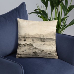 May include: A decorative throw pillow featuring a sepia-toned nautical illustration of a harbor scene with sailing ships, buildings, and mountains in the background. The pillow is square and rests on a blue surface.