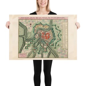 May include: An antique map of Luxembourg City, showing the city's fortifications and surrounding landscape. The map is printed in black, red, green, and brown ink on a cream-colored paper. The title "NOUVEAU PLAN DE LA VILLE DE LUXEMBOURG" is printed at the top of the map.