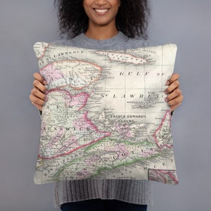 Puede incluir: Una almohada con un mapa vintage de las Provincias Marítimas de Canadá. El mapa muestra las provincias de New Brunswick, Nueva Escocia y la Isla del Príncipe Eduardo. El mapa está impreso en tonos de rosa, verde y marrón sobre un fondo blanco.