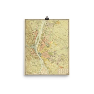 May include: A vintage map of Budapest, Hungary. The map is printed in shades of yellow, green, pink, and blue. The Danube River is shown in blue, and the city is divided into districts. The map includes text in German and Hungarian.