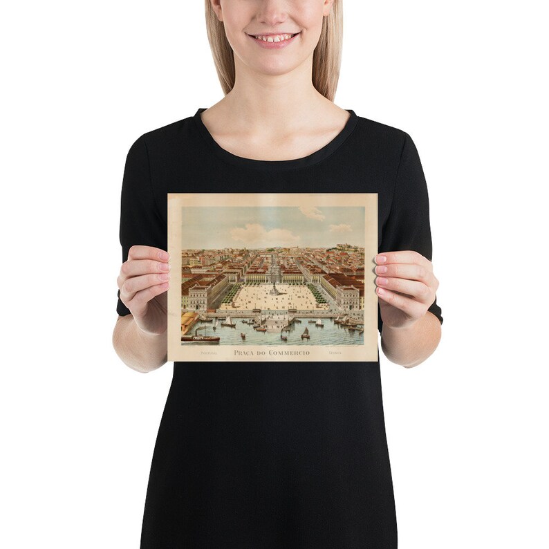 May include: A vintage print of Pra&ccedil;a do Commercio, a historic square in Lisbon, Portugal. The print features a detailed illustration of the square, with buildings, boats, and people. The print is held by a person.