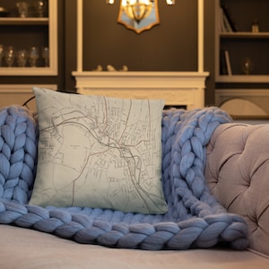 May include: A throw pillow with a vintage map of a city printed on it. The pillow is cream colored and has a light blue throw blanket on top of it.