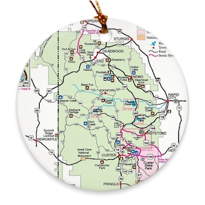 May include: A detailed map of the Black Hills National Forest in South Dakota, featuring major roads, towns, and points of interest. The map is printed on a round, white ornament.