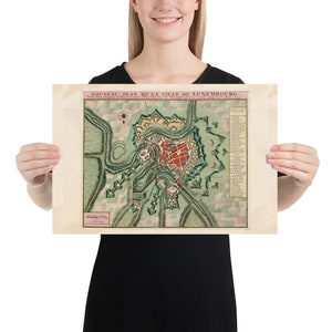 May include: A vintage map of the city of Luxembourg, printed in French, with a detailed illustration of the city's fortifications and surrounding landscape. The map is dated 1731.