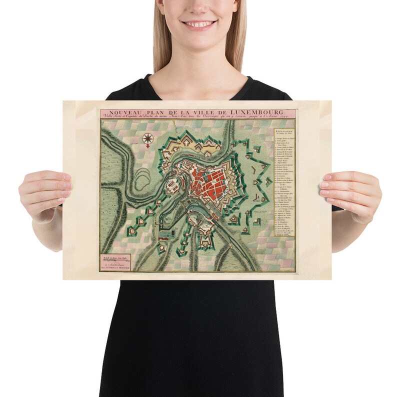 May include: A vintage map of the city of Luxembourg, printed in French, with a detailed illustration of the city's fortifications and surrounding landscape. The map is dated 1731.