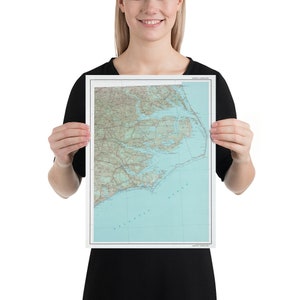 May include: A person holding a map of North Carolina. The map is printed on white paper and shows the state's coastline, rivers, and major cities. The map is framed in a white frame.