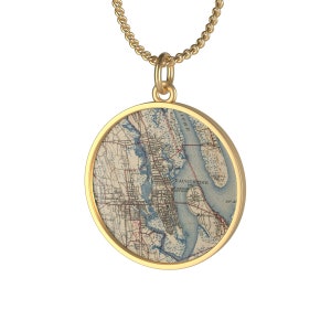 May include: Gold necklace with a round pendant featuring a vintage map of St. Augustine, Florida. The map shows the city's streets, waterways, and surrounding areas.