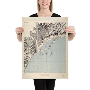 May include: A vintage map of Malaga, Spain, with a blue dot marking a location labeled "Q". The map is printed on aged paper with a light blue background and black lines.