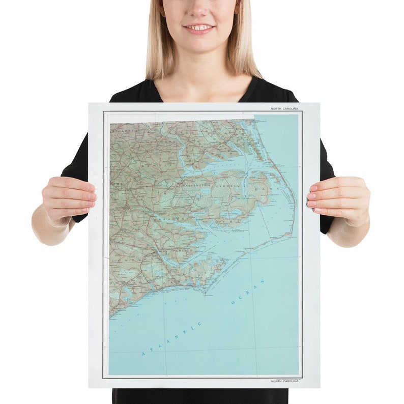 May include: A poster of a detailed map of North Carolina, showing the state's geography and coastline. The map is printed in shades of green, brown, and blue, with the Atlantic Ocean and major waterways highlighted.
