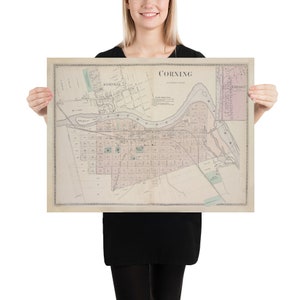 May include: A vintage map of Corning, New York, printed on aged paper with a light brown background. The map shows the city's streets, buildings, and waterways. The title "CORNING" is printed in the upper right corner of the map.