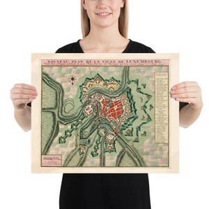 May include: A vintage map of Luxembourg City, titled "Nouveau Plan de la Ville de Luxembourg." The map is printed on a cream-colored paper with a green and pink color scheme. The map shows the city's layout with its fortifications and surrounding landscape.