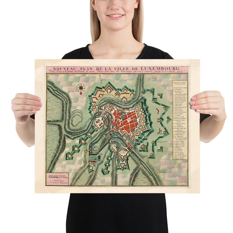 May include: A vintage map of Luxembourg City, titled "Nouveau Plan de la Ville de Luxembourg." The map is printed on a cream-colored paper with a green and pink color scheme. The map shows the city's layout with its fortifications and surrounding landscape.