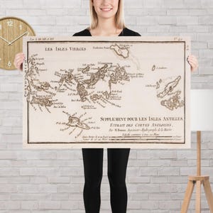 Op de afbeelding: Een ingelijste vintage kaart van de Maagdeneilanden, met gedetailleerde cartografie en tekst in het Frans. De kaart is gedrukt in sepiatinten en wordt door een persoon vastgehouden. De kaart bevat de tekst "LES ISLES VIERCES".