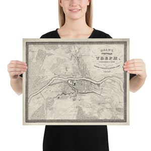 May include: A vintage map of the city of Tver, Russia, printed in 1842. The map is in black and white and shows the city's streets, buildings, and landmarks. The map is framed and displayed on a wall.