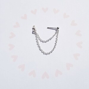 May include: Silver chain earring with a small ball at the end. The chain is double-layered and hangs from a small stud.