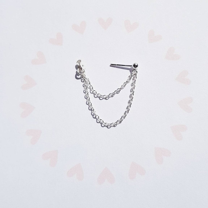 May include: Silver chain earring with a small ball at the end. The chain is double-layered and hangs from a small stud.