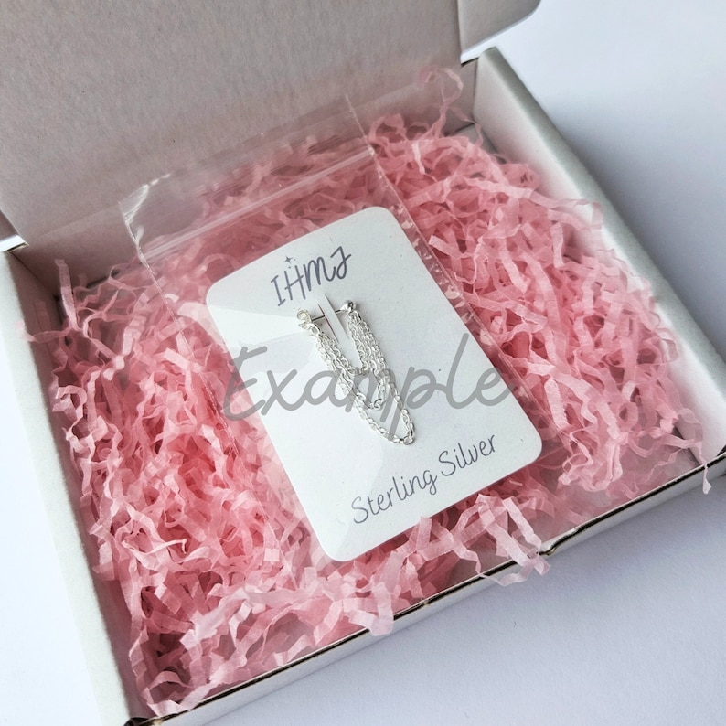 May include: A pair of sterling silver chain earrings in a clear plastic bag on a white card with the text "IHMz Example Sterling Silver". The bag and card are in a white box with pink crinkle paper.