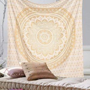May include: A white tapestry with a large gold mandala design. The mandala has intricate details and a circular pattern. The tapestry is hanging on a wall and there are pillows and a cushion in front of it.