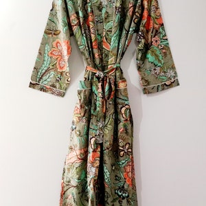 Op de afbeelding: Een groene badjas met een bloemenprint en witte bies. De badjas heeft een strikceintuur en lange mouwen.