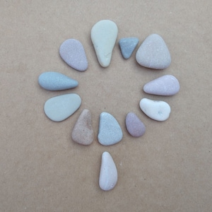 Może przedstawiać: Kolekcja gładkich, szarych, brązowych i fioletowych kamieni ułożonych w okrąg na brązowej powierzchni.